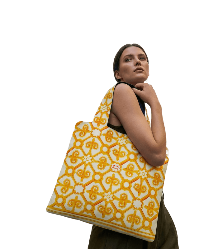 A person with long hair looks upward, confidently holding the Shine at Heart yellow and white patterned tote bag over their shoulder against a white background.